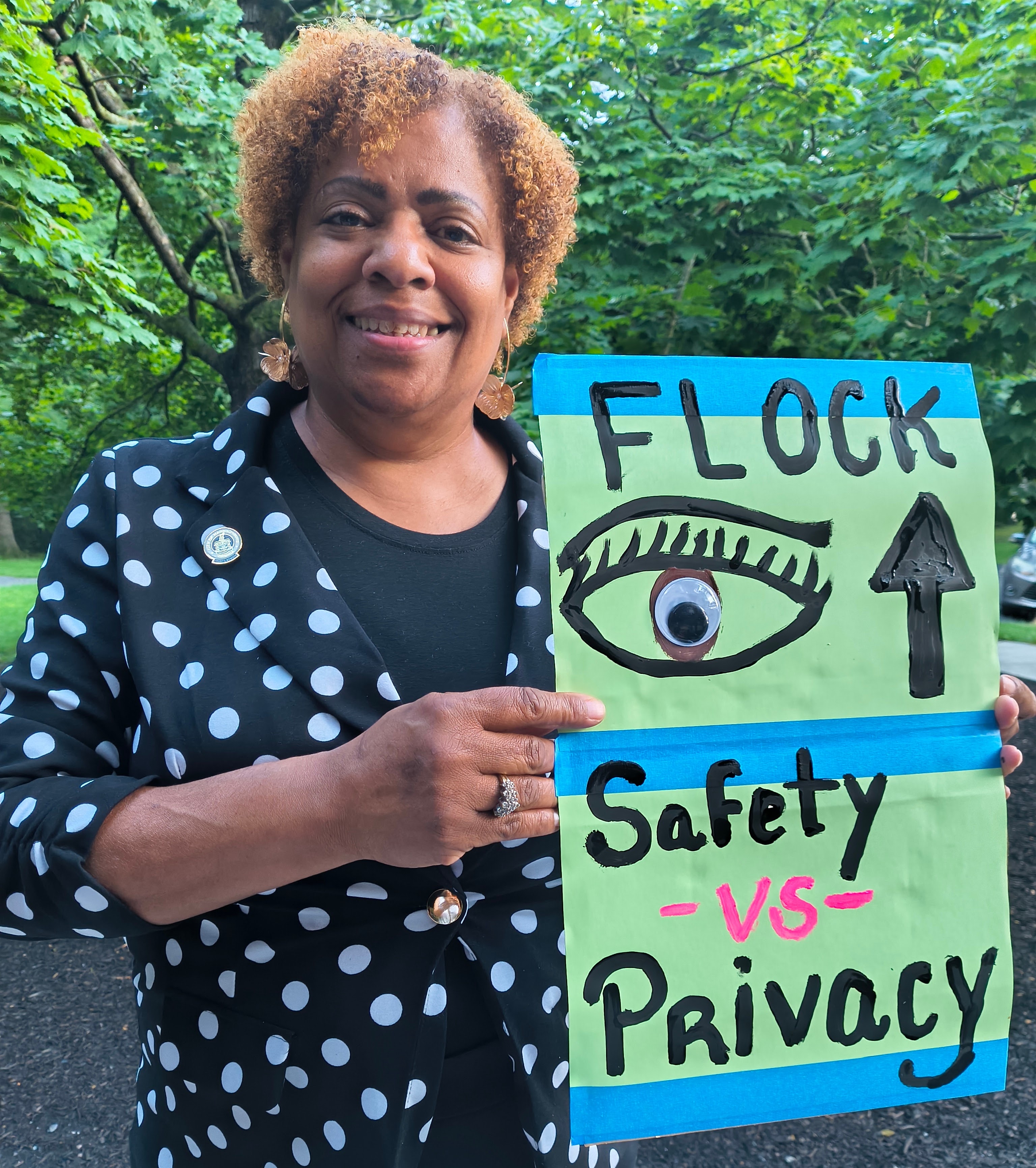 Monica Robinson holding a handmade Flock Safety and Privacy sign outdoors