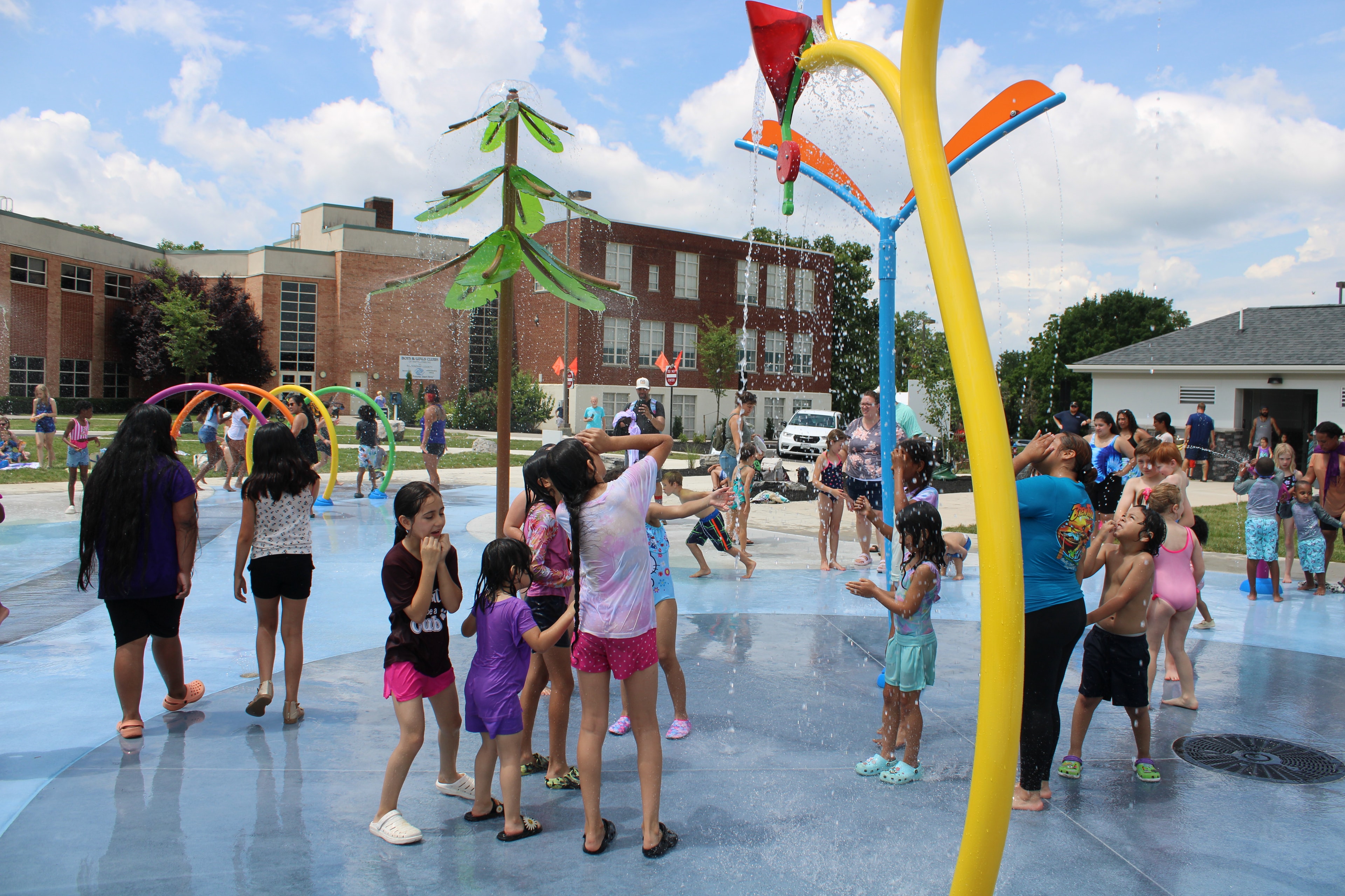 Children and families enjoying a colorful public splash pad on a sunny day.